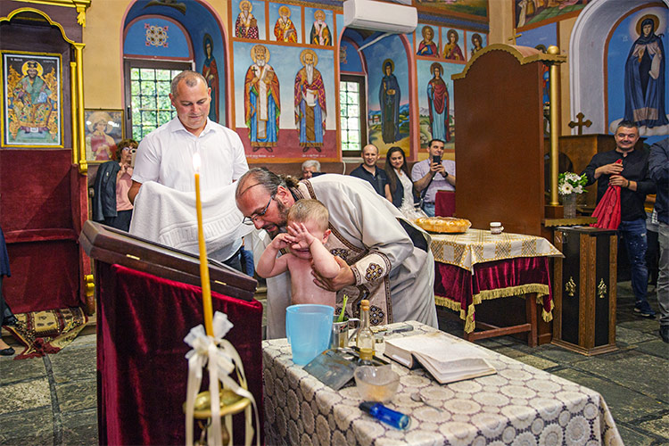 Отецът кръщава момченце в купела по време на ритуал Свето Кръщение в Белащински манастир Свети Георги Победоносец.