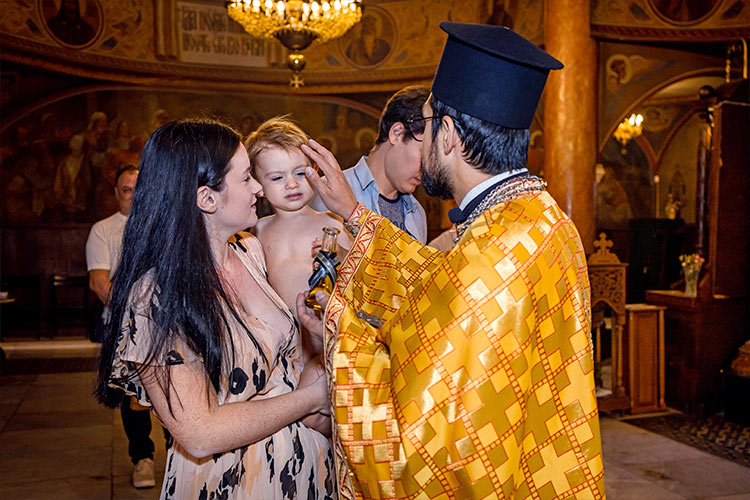 Отецът помазва момченцето по челцето преди кръщаването в купела по време на ритуал Свето Кръщение в катедрален храм Света Богородица, град Пловдив.