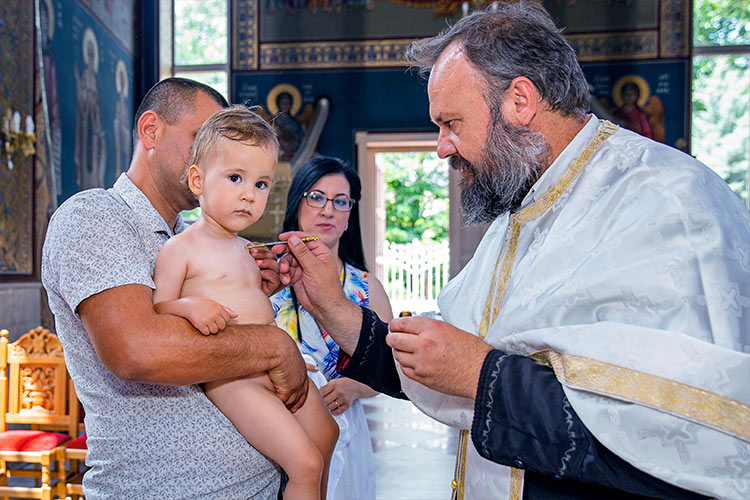 Отецът помазва момченцето с елей след кръщаване в купела по време на ритуал Свето Кръщение в храм Свети Николай Мирликийски Чудотворец, град Пловдив.
