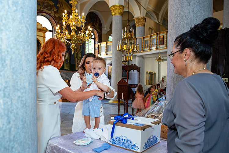 Кръстницата облича новопокръстено момченце след кръщаване в купела по време на ритуал Свето Кръщение в храм Свети Георги, град Пловдив.