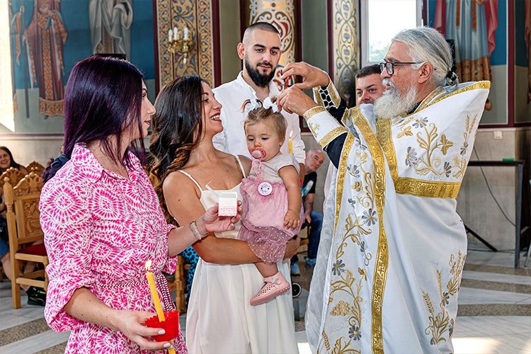 Отецът отрязва кичур коса от новопокръстено момиченце по време на ритуал Свето Кръщение в храм "Свети Николай Мирликийски Чудотворец", град Пловдив.