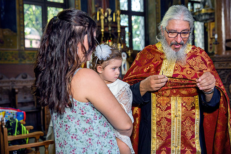 Отецът отрязва кичур коса от новопокръстено момиченце по време на ритуал Свето Кръщение в храм "Света Преподобна Петка", град Пловдив.