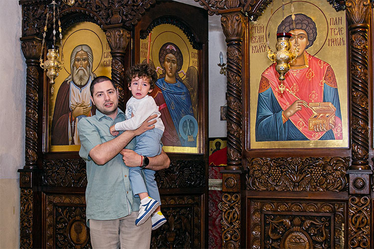 Новопокръстено момченце гушнато от баща си излиза от олтара след ритуална обиколка по време на ритуал Свето Кръщение в храм Свети Клиемнт Охридски, град Пловдив.