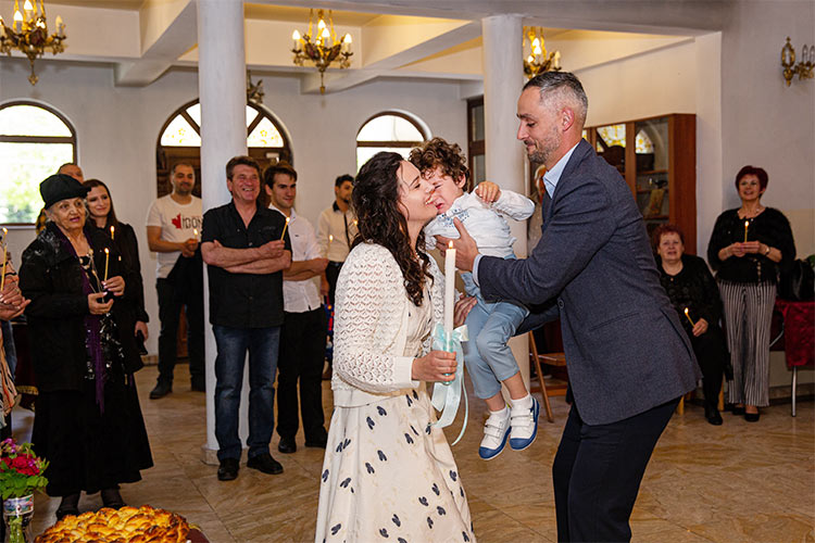 Кръстникът предава новопокръстено момченце на майката по време на ритуал Свето Кръщение в храм Свети Клиемнт Охридски, град Пловдив.
