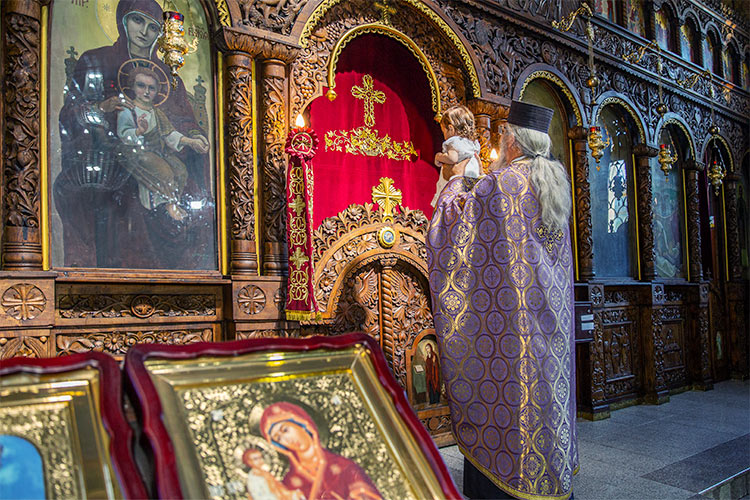 Отецът представя новопокръстено момиченце пред олтара по време на ритуал Свето Кръщение в храм Света Преподобна Петка, град Пловдив.