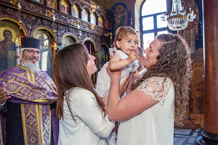 Кръстницата предава новопокръстеното момиченце на майка му по време на ритуал Свето Кръщение в храм Света Преподобна Петка, град Пловдив.