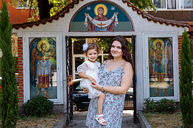 Кръстницата с новопокръстеното момиченце след края на кръщението му в двора на храм Света Преподобна Петка, град Пловдив.