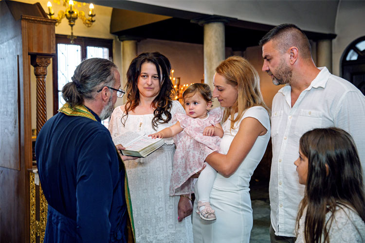 Момиченце хванало требника, от който отеца чете молитва по време на кръщението ѝ в храм Света Троица, Кръстова Гора.