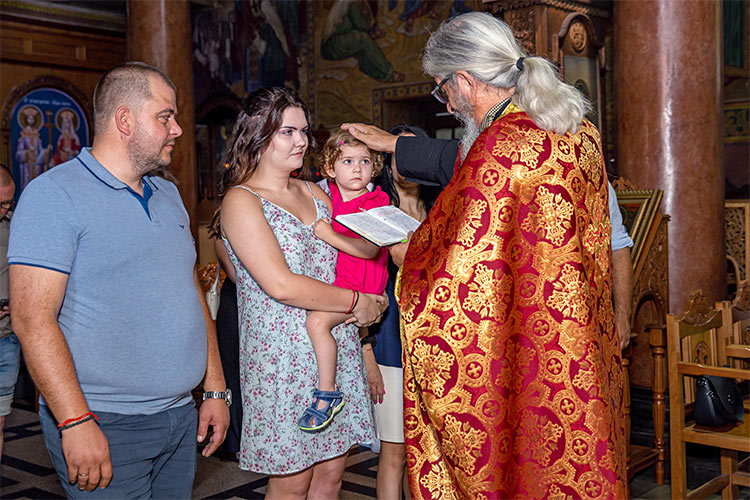Отецът възлага ръка върху главата на момиченцето по време на ритуал Свето Кръщение в храм Света Преподобна Петка, град Пловдив.