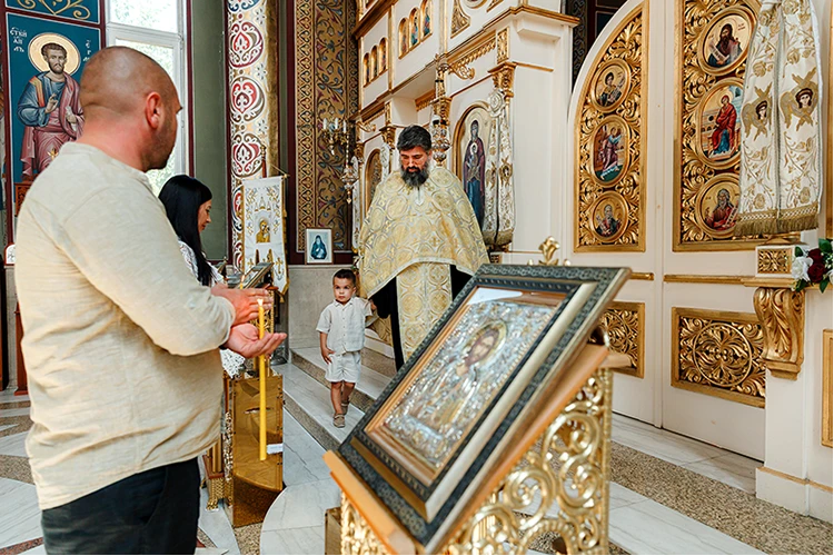 Отецът предава детето на кръстниците в края на ритуал Свето Кръщение.